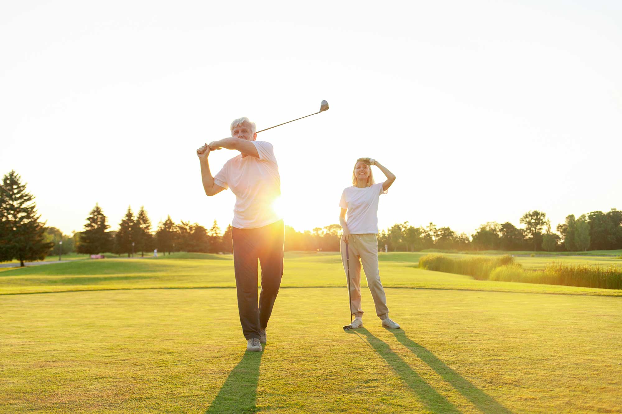 elderly-senior-couple-in-uniform-playing-golf-on-golf-course-at-sunset
