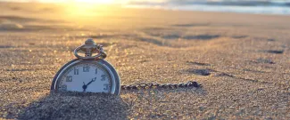 Pocket watch nestled in the sand of a beach at sunset